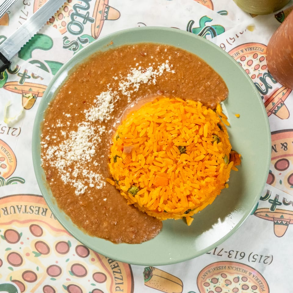 Mexican plate with orange rice and refried beans topped with crumbled white cheese, beside a red drink.