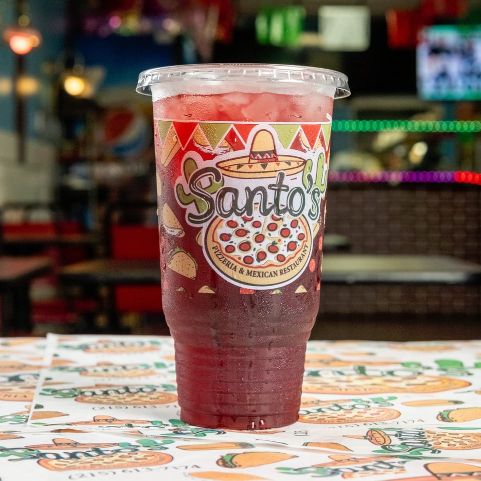 Cold red drink in a branded Santo’s Pizzeria and Mexican Restaurant cup on a colorful restaurant table.