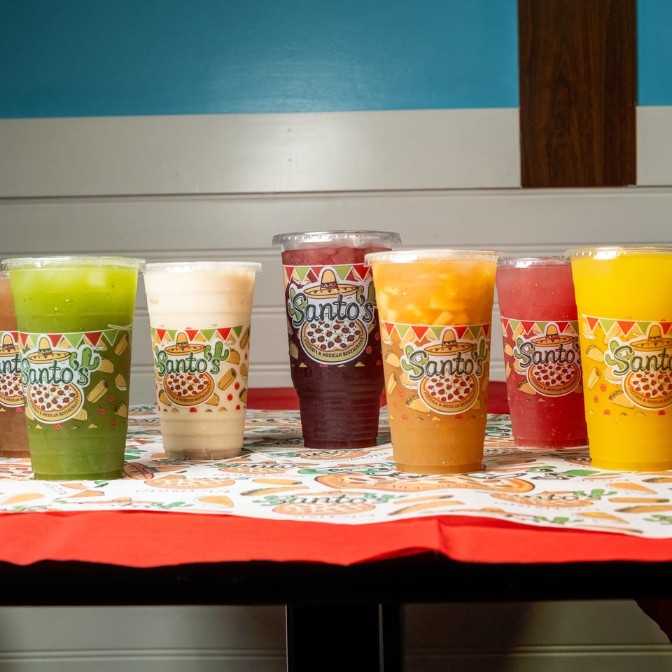 Six colorful drinks in branded Santo’s cups displayed on a festive Mexican restaurant table.