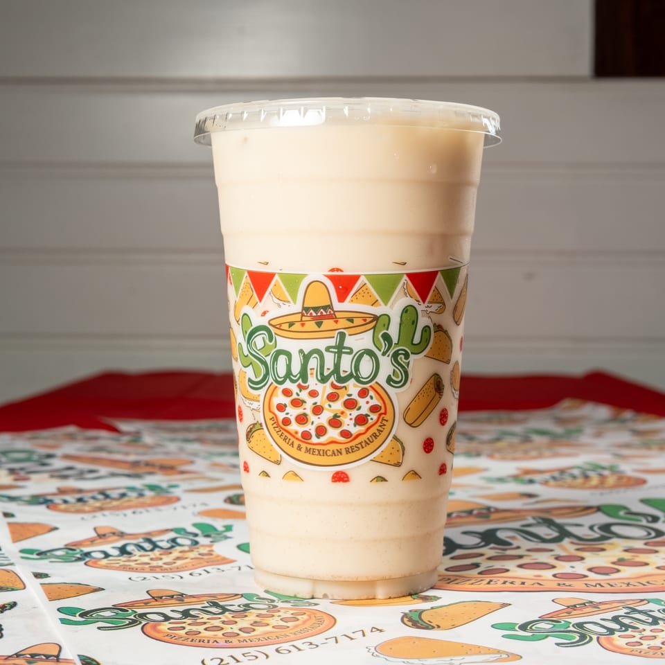 Creamy beverage in a Santos-branded cup sits on a colorful pizzeria and Mexican restaurant table covering.