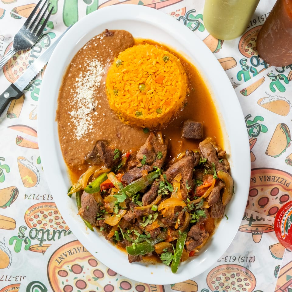 Mexican platter with orange rice, refried beans, and grilled beef with peppers, onions, and cilantro, alongside colorful beverages.