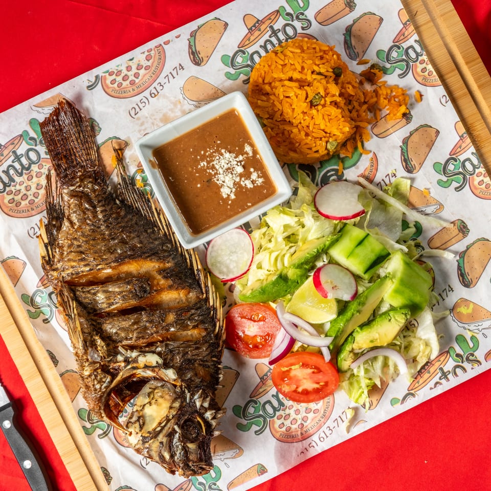 Grilled whole fish served with Mexican rice, refried beans, and a fresh salad of lettuce, avocado, radishes, cucumber, and tomatoes.